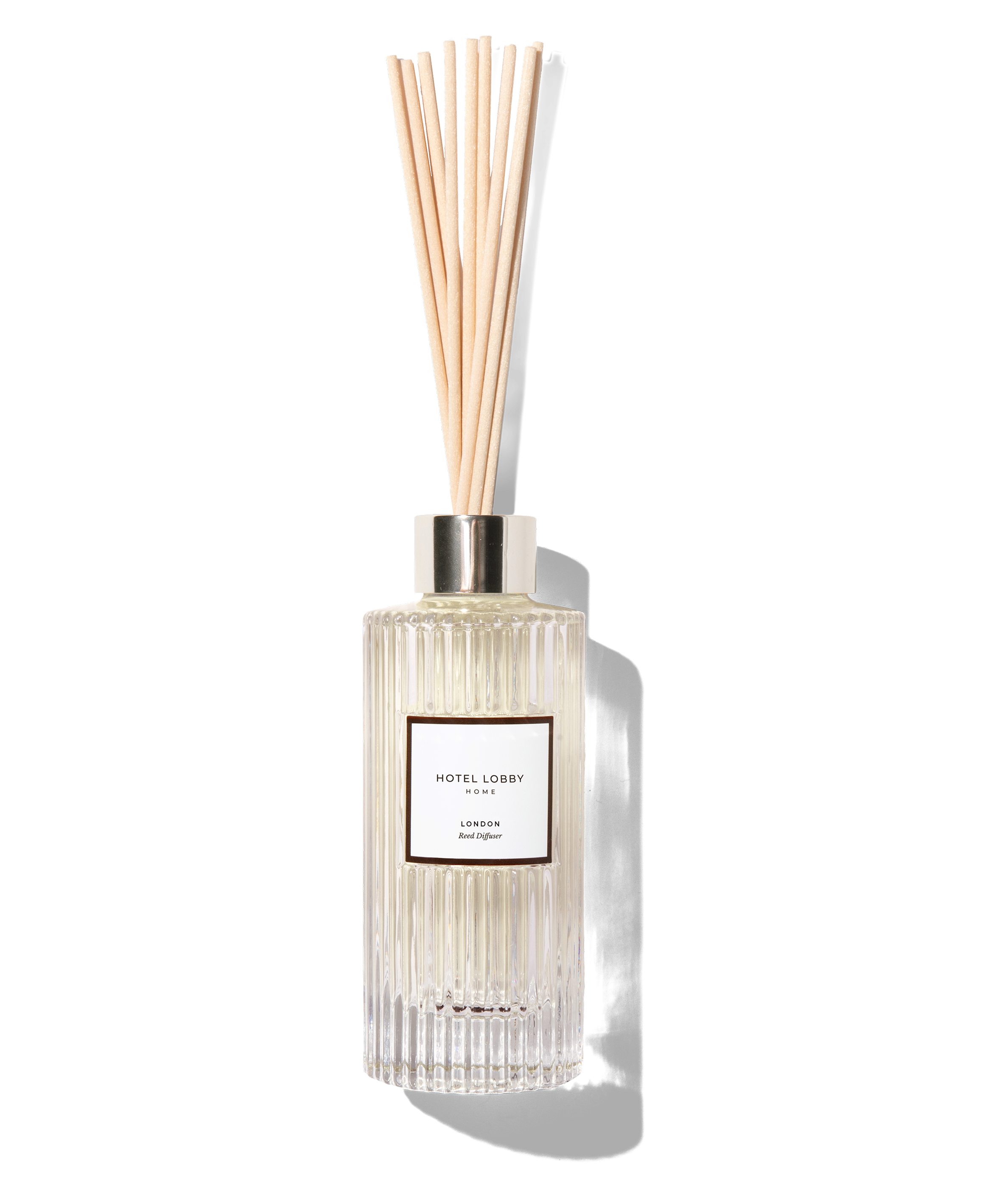 A glass reed diffuser with wooden sticks against a beige background.